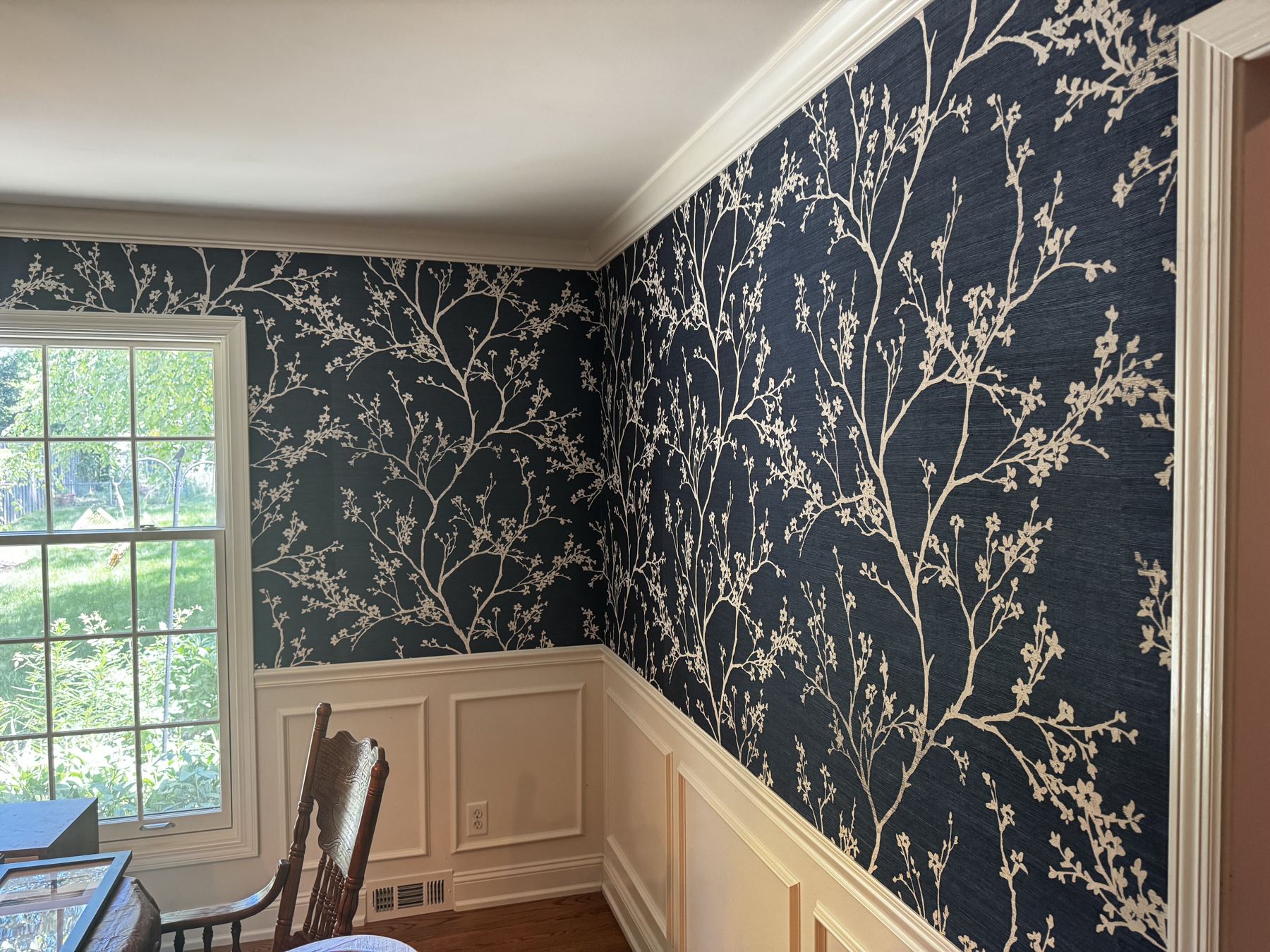 Navy grasscloth with cream branches installed in a dining room above white wainscoting